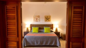 A hotel room with a large bed, two nightstands, a wooden headboard, and two wall art pieces. - TOT Punta Cana Apartments (Punta Cana)
