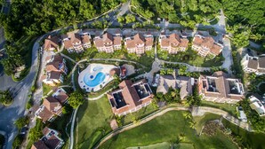 An aerial view of a residential area with multiple houses, a central swimming pool, and well-maintained lawns. - TOT Punta Cana Apartments (Punta Cana)