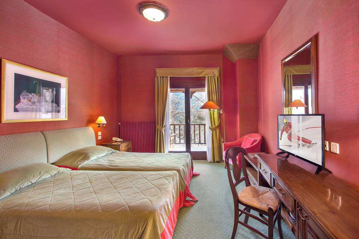 A hotel room with two beds, a desk, a chair, a television, and a window with curtains.