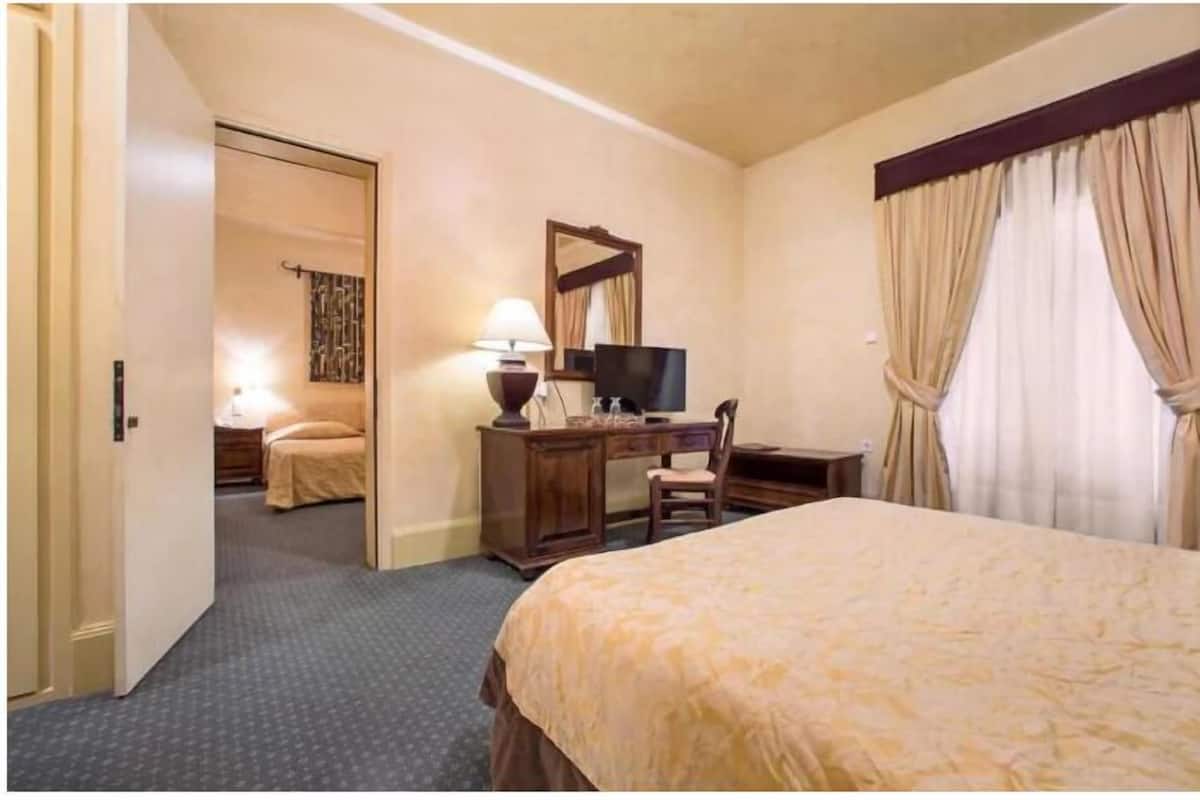 A hotel room with a bed, a desk with a chair, a television, and a door leading to another room.