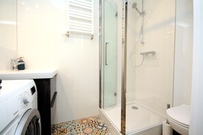 A modern bathroom with a glass-enclosed shower, a washing machine, and a toilet.
