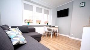 Un salon moderne avec un canapé gris, une table à manger et un téléviseur fixé au mur.