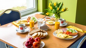 A breakfast table with plates of food, a vase of flowers, and a window view. - Sport Hotel (Liepaja)