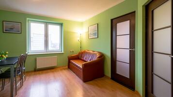 A room with a brown leather sofa, a dining table with chairs, a window with blinds, and a door with a frosted glass panel.