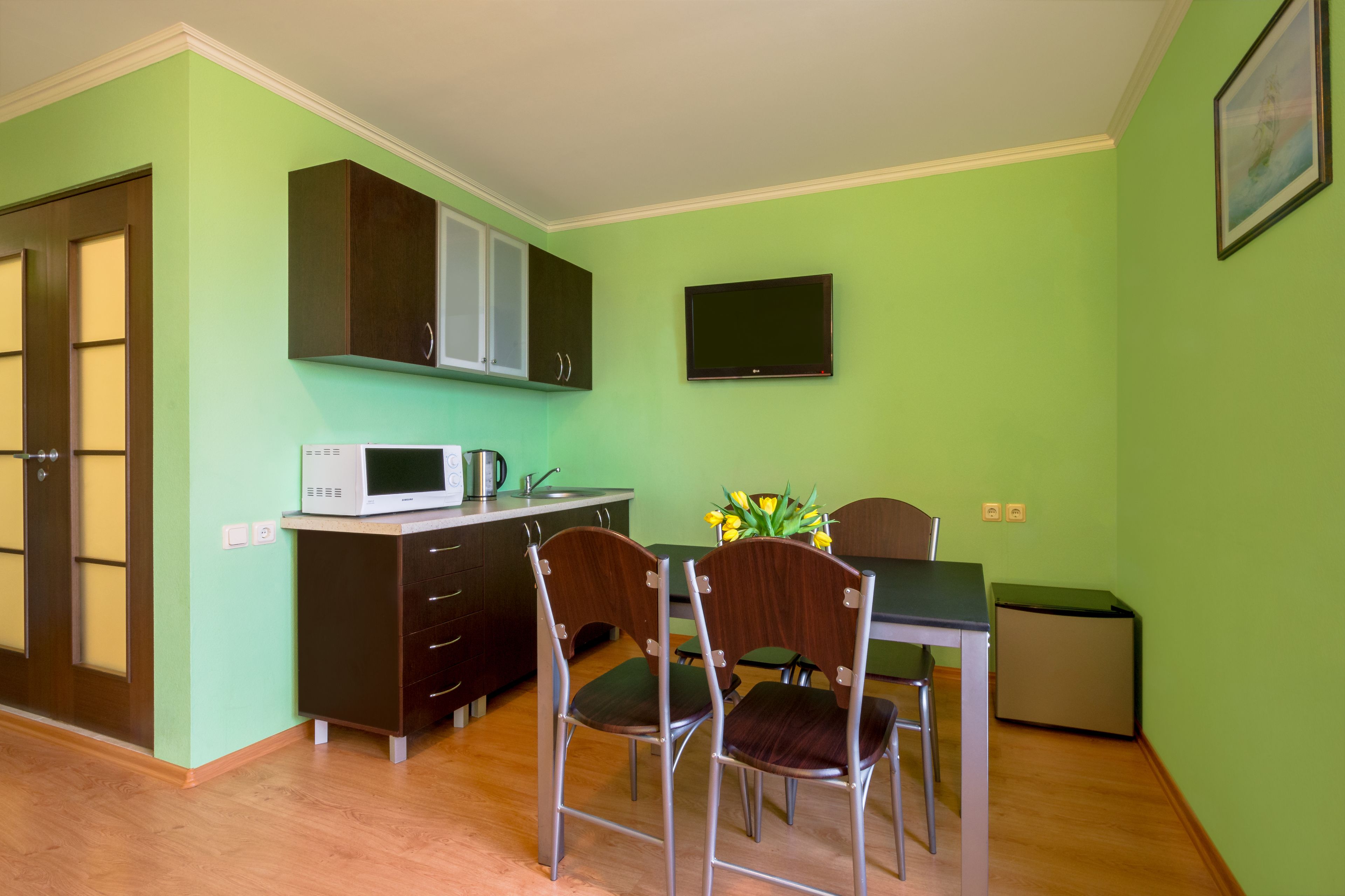 A compact kitchen with a microwave, stove, and cabinets. There are two chairs and a small table.