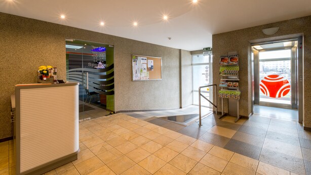 A hotel reception area with a reception desk, a bulletin board, a glass door leading outside, and a vending machine. - Sport Hotel (Liepaja)