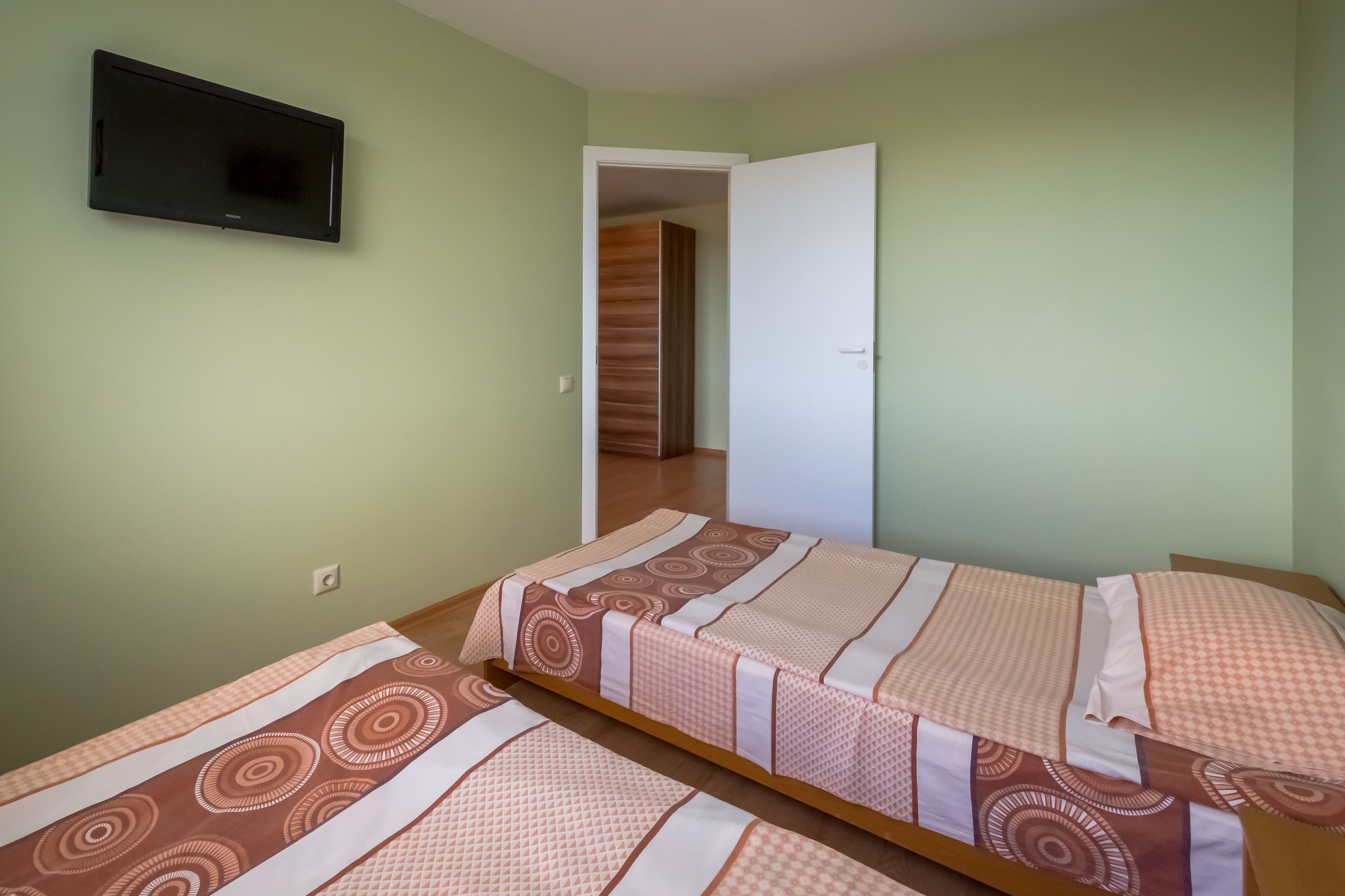 A room with two beds, a television on the wall, and a door leading to another room.