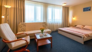 A hotel room with a bed, a sofa, a chair, a small table with a vase of flowers, and a window with curtains. - Sport Hotel (Liepaja)