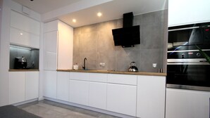 A modern kitchen with white cabinets, a built-in oven, a microwave, and a flat-screen TV mounted on the wall. - Rent a Flat apartments - Kilińskiego St. (Gdansk)
