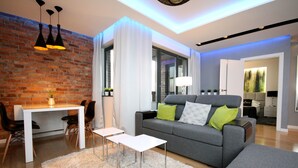 A modern living room with a grey sofa, white coffee table, and a dining area with a white table and chairs. - Rent a Flat apartments - Kilińskiego St. (Gdansk)