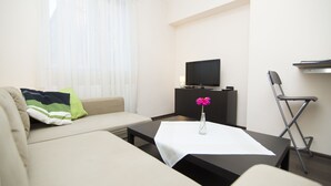 A modern living room with a sofa, a coffee table, a TV on a stand, a chair, and a small table with a vase of flowers. - Rent a Flat apartments - Korzenna St. (Gdansk)