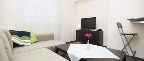 A modern living room with a sofa, a coffee table, a TV on a stand, a chair, and a small table with a vase of flowers.