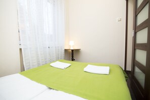 Et hotelværelse med seng, natbord, lampe og et vindue med gardiner.