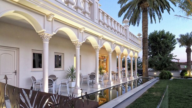 A hotel with a covered outdoor seating area, palm trees, and a pool. - Quinta Real Granada (Huetor Vega)