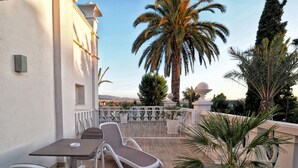 A terrace with a table and chairs, a palm tree, and a view of the city. - Quinta Real Granada (Huetor Vega)