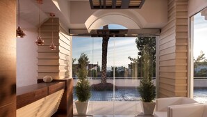 A modern interior with a wooden reception desk, a glass door leading outside, and a seating area with a view of the outdoors. - Quinta Real Granada (Huetor Vega)
