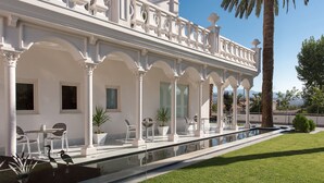 A white building with a pool, outdoor seating, and palm trees. - Quinta Real Granada (Huetor Vega)