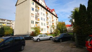 Um edifício residencial com várias andares, varandas, carros estacionados e céu azul.