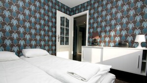 Quarto de hotel com uma cama, penteadeira e porta que dá para outro quarto.