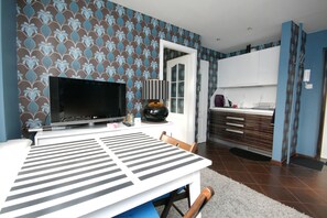 A dining area with a TV, a table with a striped tablecloth, and a kitchen in the background. - Rent a Flat apartments - Mazurska St. (Gdansk)