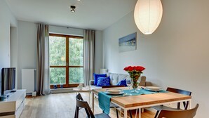 A modern living room with a dining area, large windows, a sofa with blue cushions, and a table set for two.