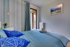 Quarto com cama, cortinas, luminária na parede, um quadro e uma janela.