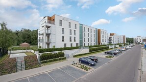 A modern multi-story residential building with balconies, a parking lot, and a landscaped area.