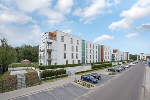 A modern multi-story residential building with balconies, a parking lot, and a landscaped area.