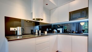 A modern kitchen with white cabinetry, a stainless steel kettle, and a built-in microwave.