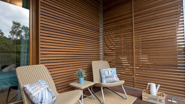 A modern outdoor seating area with wicker chairs, a small table, and a wooden slatted wall.