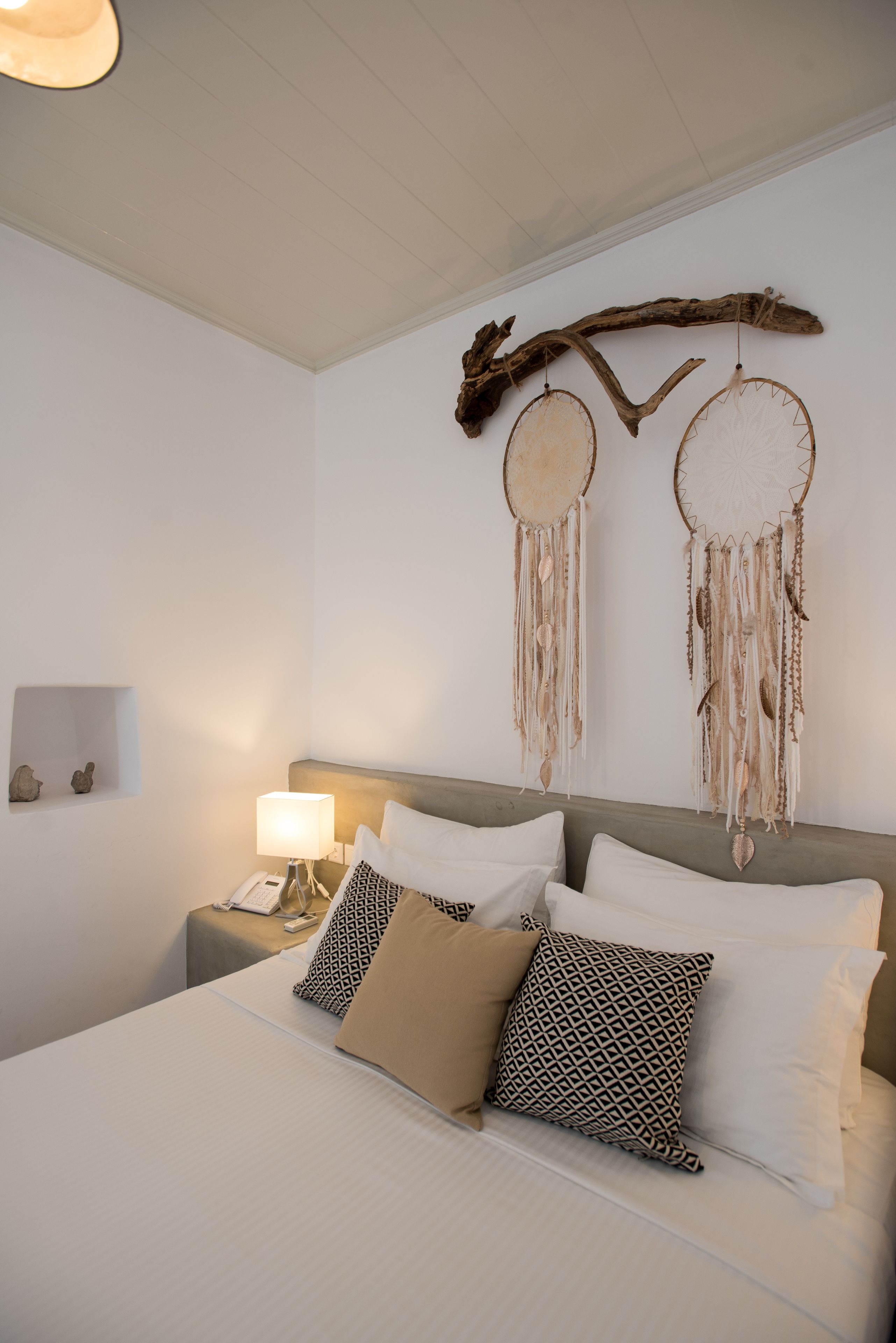 A neatly made bed with patterned pillows, a bedside lamp, and a wall-mounted dreamcatcher.