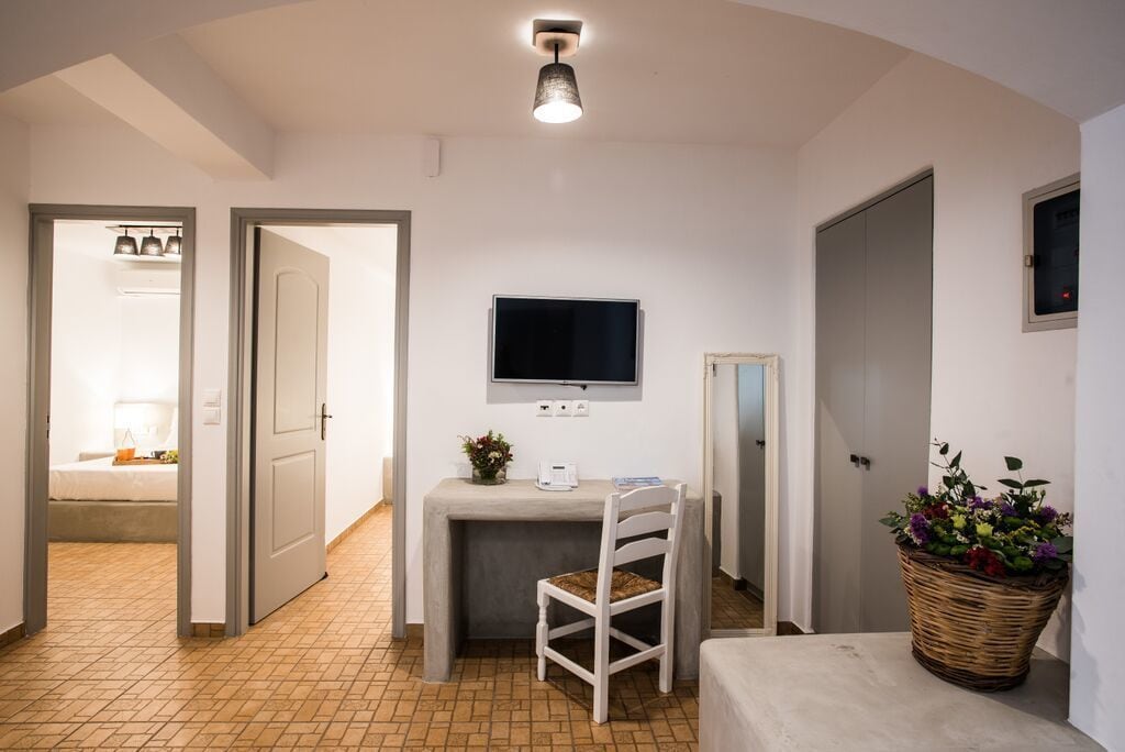A compact room with a desk, chair, television, and a large woven basket of flowers.