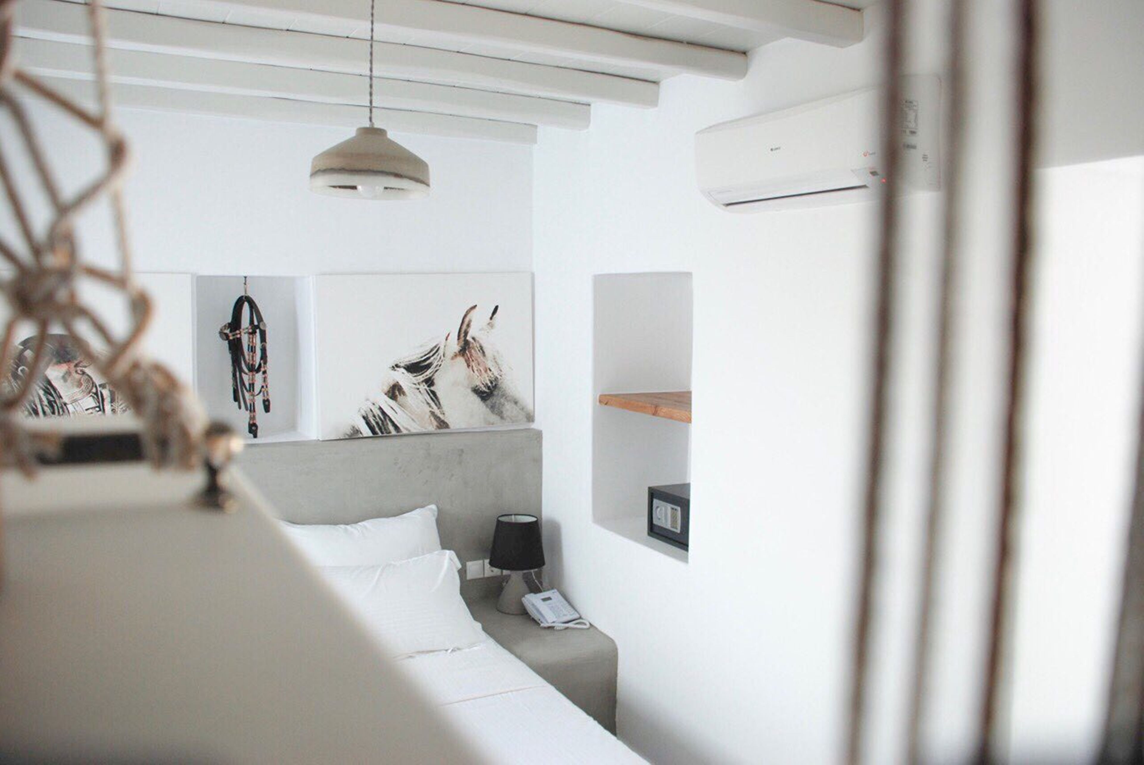A modern hotel room with a bed, bedside table, lamp, and artwork on the wall.