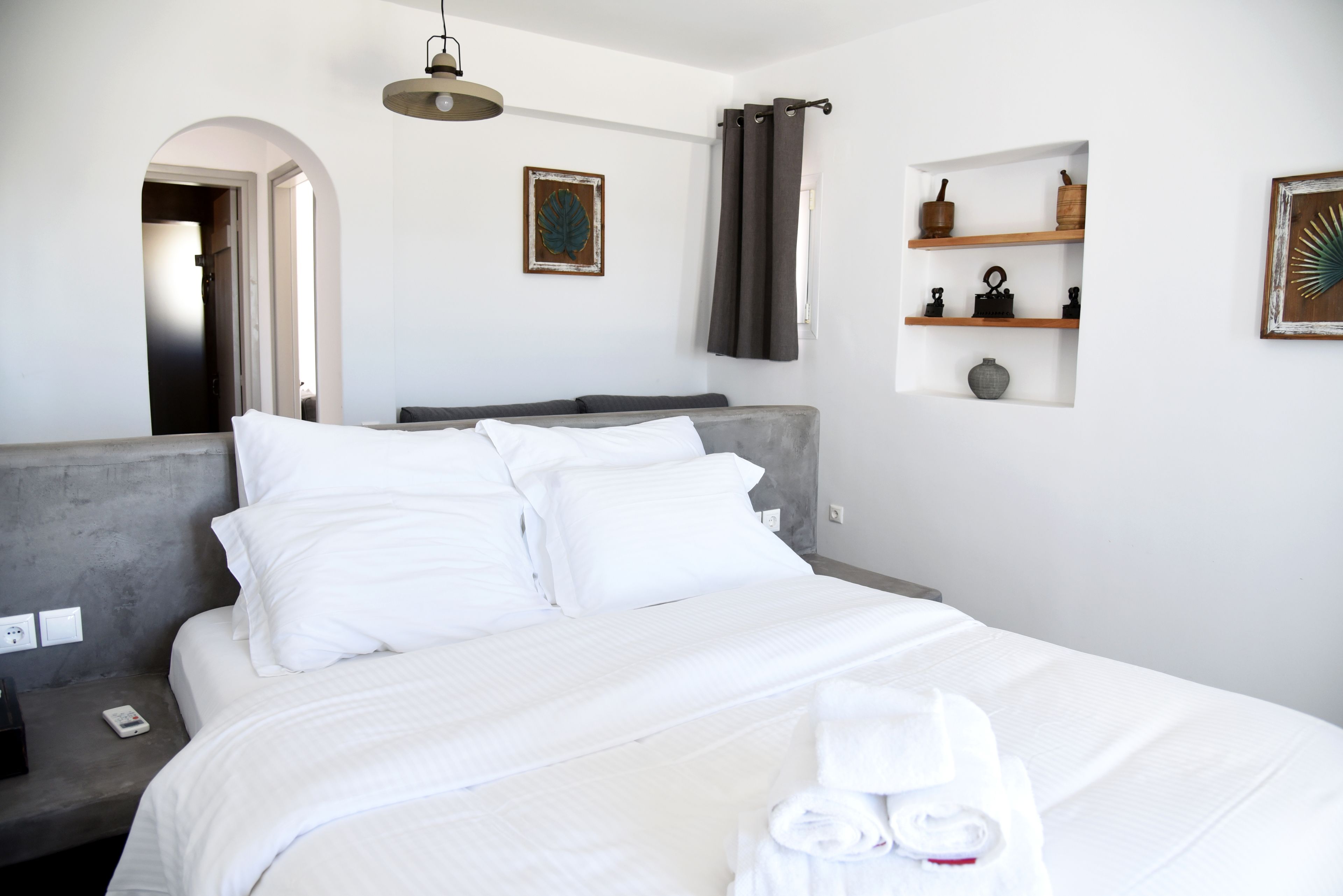 Habitació d'hotel moderna amb un llit gran, un reposacapses, una petita estant amb objectes decoratius i un quadre a la paret.