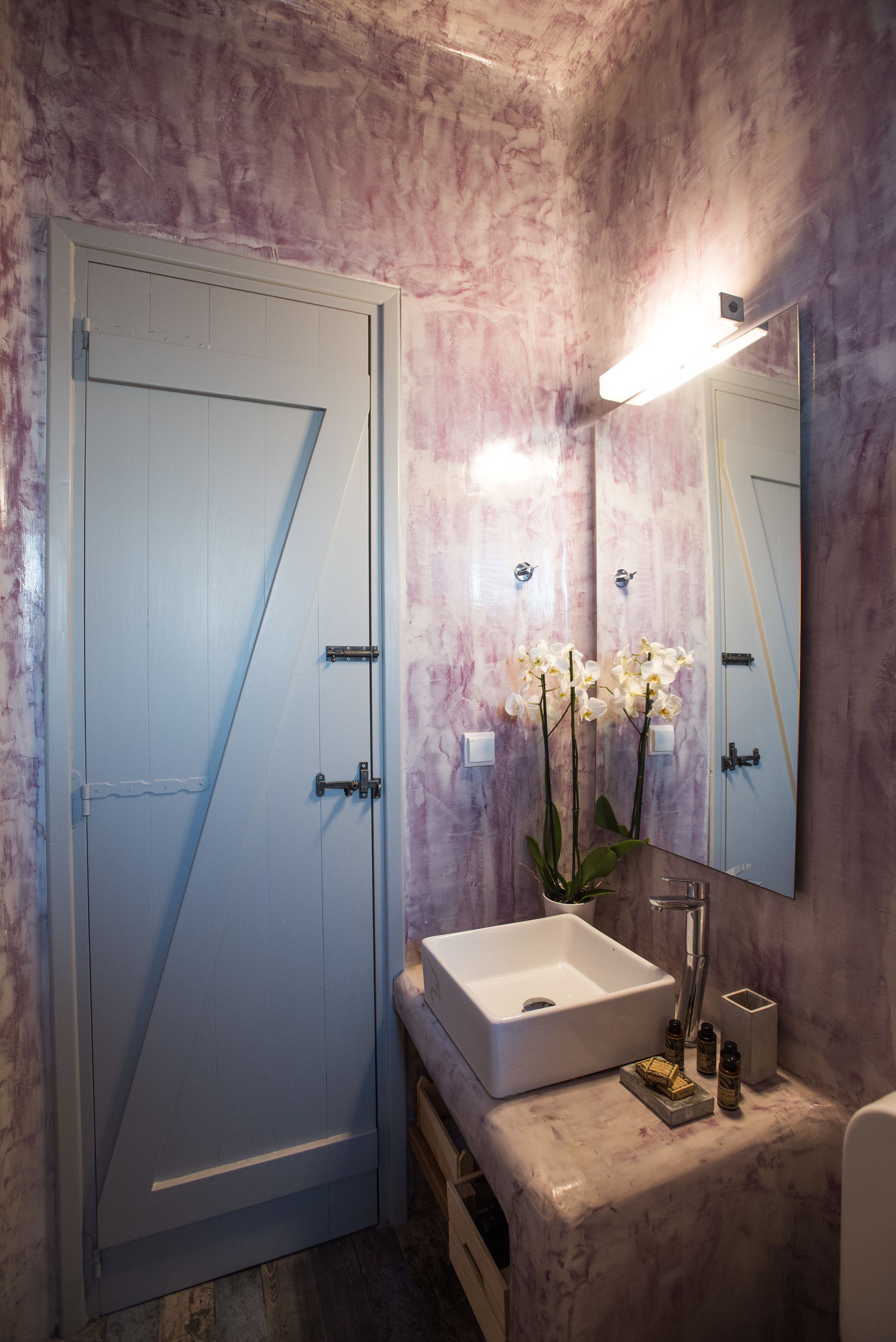 A bathroom with a white door, a white sink, a mirror, and white orchids.