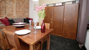 A dining area with a wooden table set for two, a vase with flowers, and a brick wall in the background. - Rent a Flat apartments - Ogarna St. (Gdansk)
