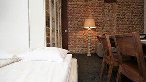A hotel room with a brick wall, a bed with white linens, a desk with a lamp, and a chair. - Rent a Flat apartments - Ogarna St. (Gdansk)
