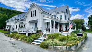 Une maison blanche à deux étages, dotée d’un porche, d’une pelouse devant et d’une boîte aux lettres.