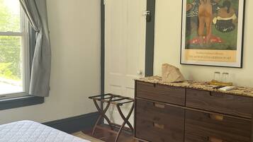 A bedroom with a bed, a dresser, a small stool, a painting, and a window with curtains.
