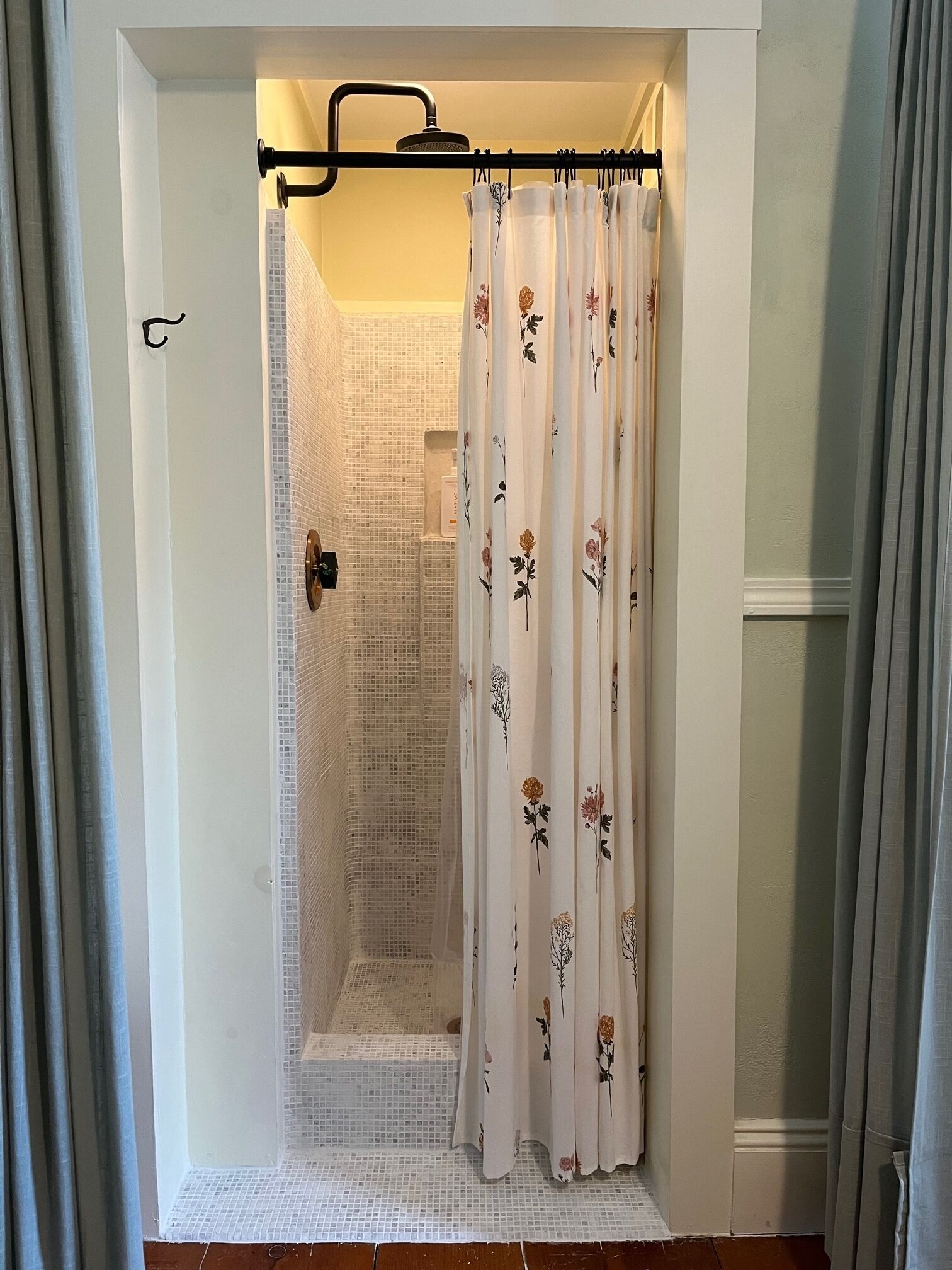 Un área de ducha con puerta de vidrio, alcachofa de ducha y cortina con motivos florales.