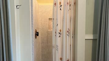 Un área de ducha con puerta de vidrio, alcachofa de ducha y cortina con motivos florales.