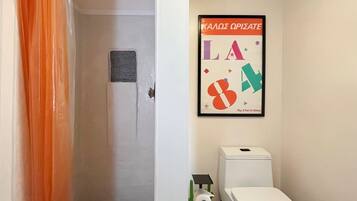 Un baño con ducha, inodoro y un cartel enmarcado en la pared.