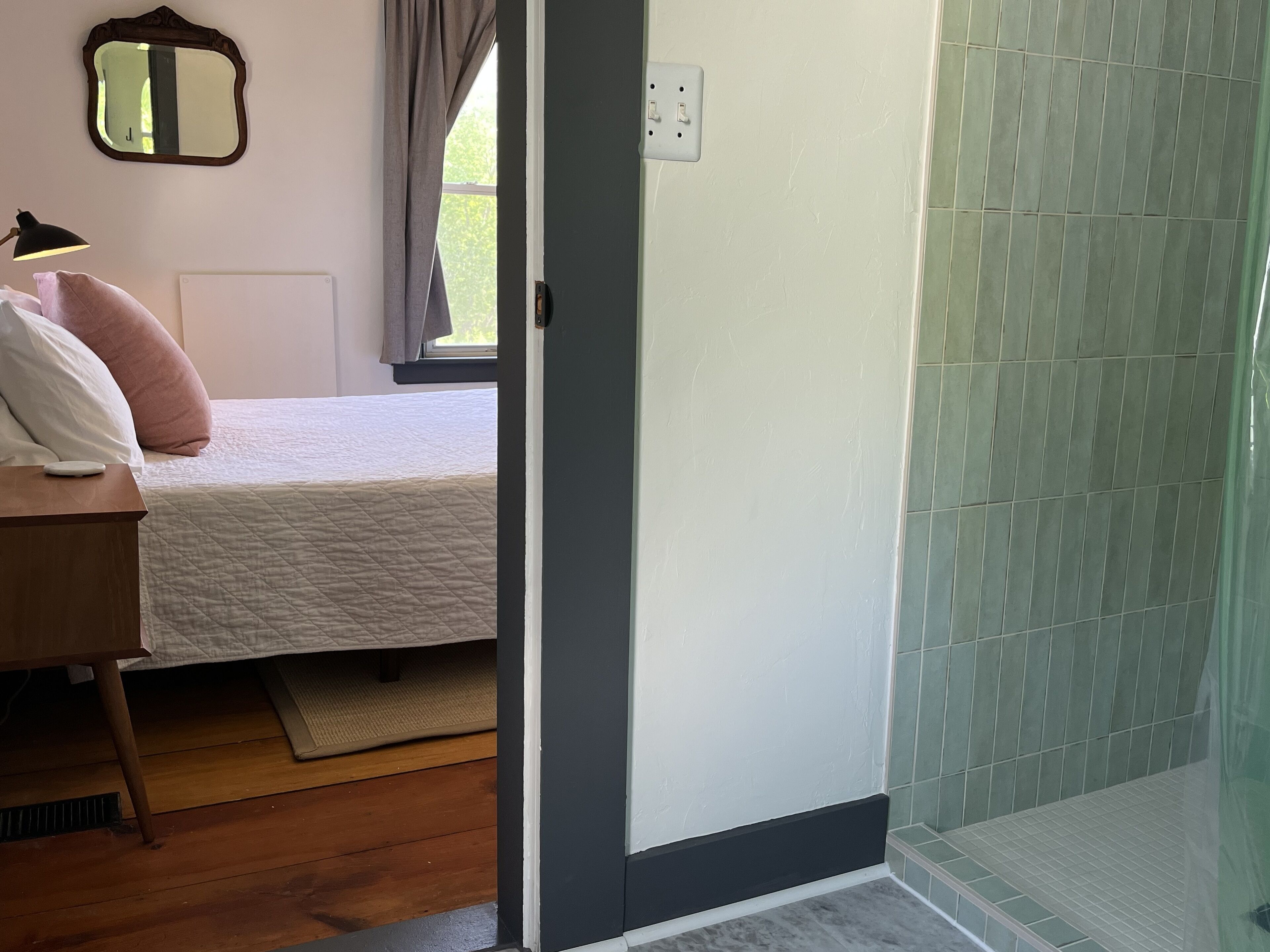 Un dormitorio con cama, mesita de noche, lámpara y un espejo en la pared.