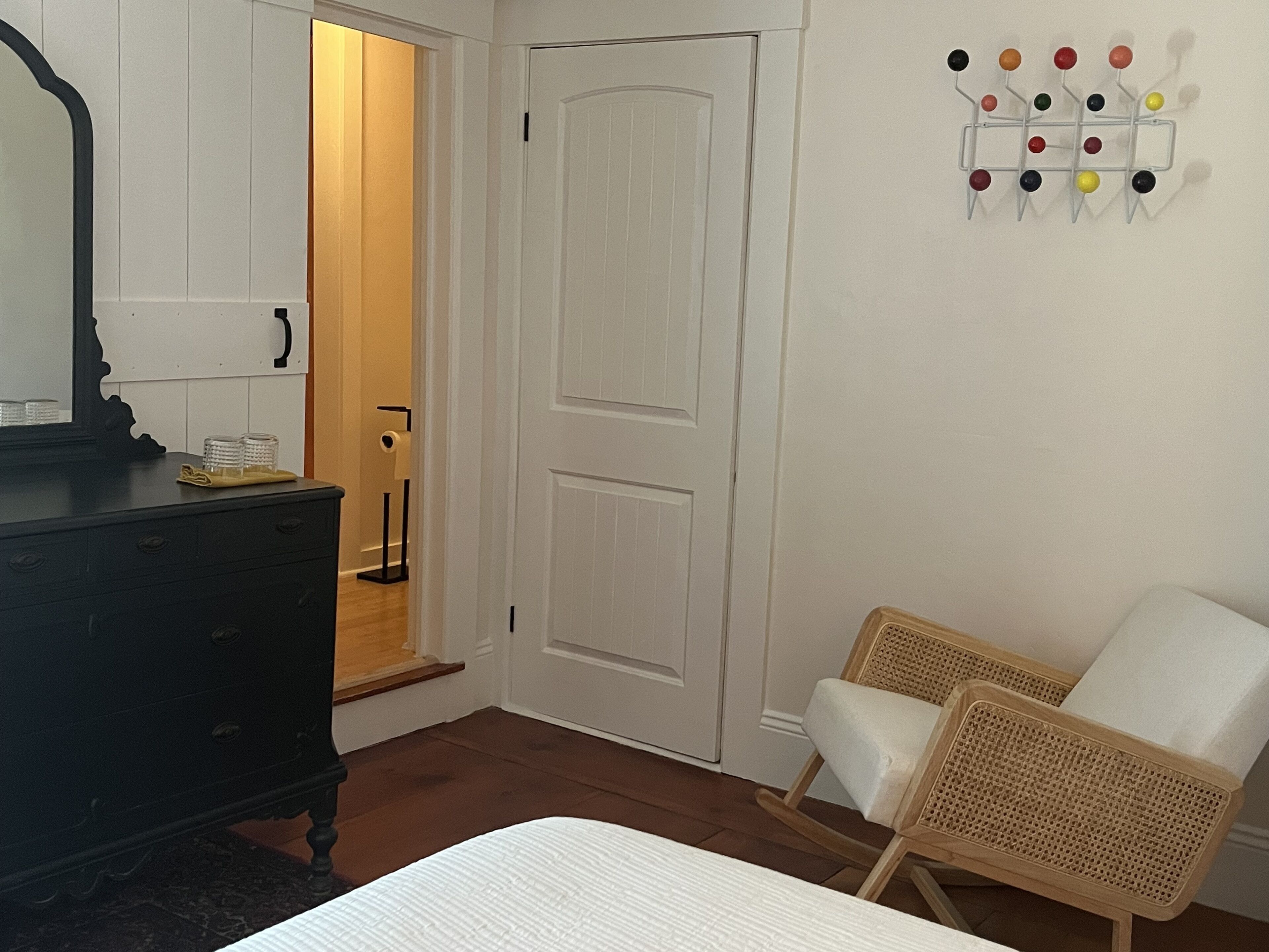Un dormitorio con cama, cómoda, silla y puerta con interruptor de luz.