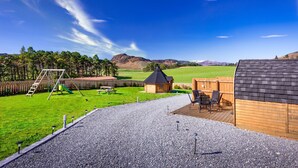 A backyard with a wooden deck, a swing set, and a small wooden cabin. - Tigh an Each B&B & Laggan Glamping (Newtonmore)