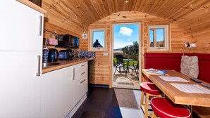 A compact kitchen with wooden walls, a dining area with red chairs, and a view of the outdoors. - Tigh an Each B&B & Laggan Glamping (Newtonmore)