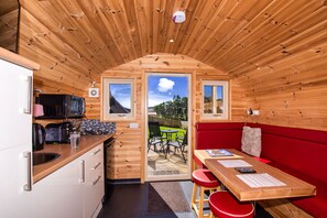A compact wooden cabin with a kitchenette, a dining area with a red couch, and a view of the outdoors through a door. - Tigh an Each B&B & Laggan Glamping (Newtonmore)