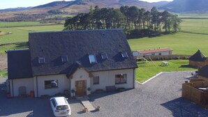A house with a sloped roof, a front porch, and a car parked in the driveway. - Tigh an Each B&B & Laggan Glamping (Newtonmore)