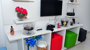 Una sala de estar moderna con un televisor de pantalla plana, una cafetera y diversos objetos decorativos en estantes.