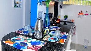 Un comedor con una mesa negra, mantel colorido y un florero con flores azules.